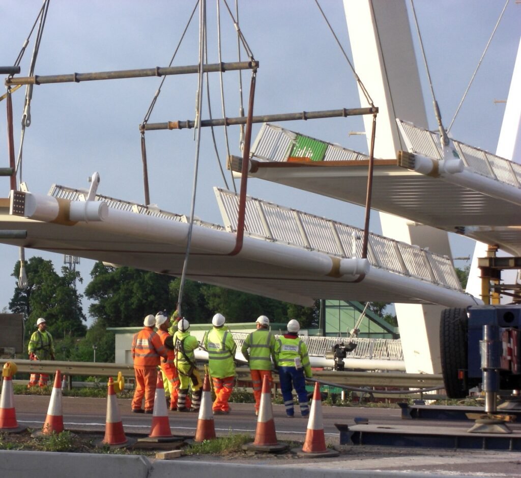 Section de tablier de pont levée à la grue au-dessus d'un giratoire, ouvriers en gilets de sécurité.