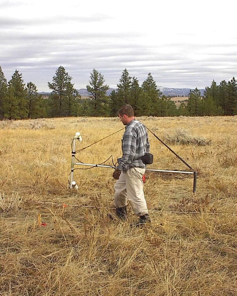 Technicien réalisant un relevé de détection au sol dans un champ, à l'aide d'un détecteur électromagnétique.