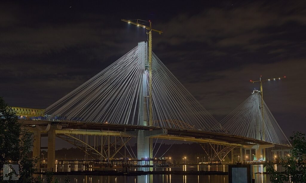 Pont à haubans en construction illuminé de nuit, avec ses grues.